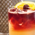 Crafted specialty cocktail with lemon and a cherry on a stick.
