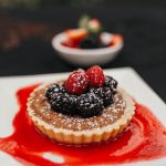 A berry tart dessert at Walters Restaurant on a white plate with a red candied shell underneath it.