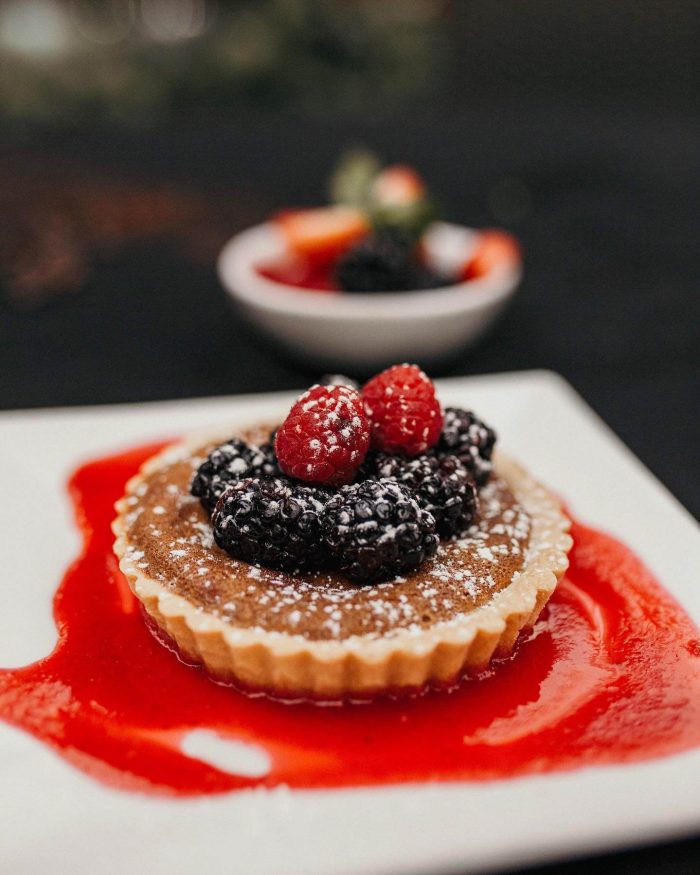 A berry tart dessert at Walters Restaurant on a white plate with a red candied shell underneath it.